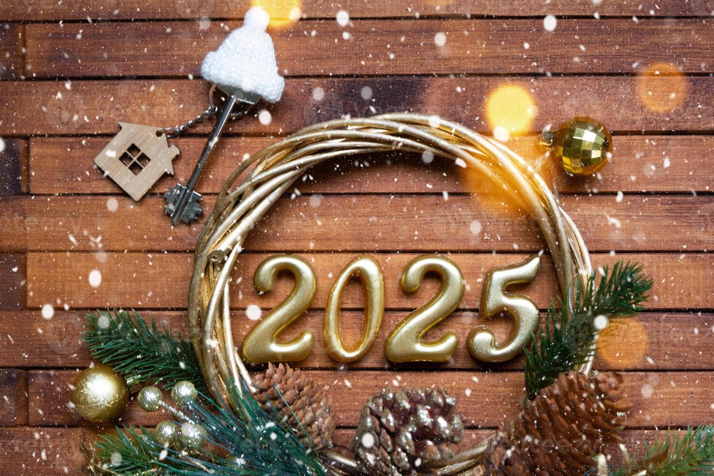 New Year House key with keychain cottage on festive brown wooden background with number 2025 in wreath, lights of garlands. Purchase, construction, relocation, mortgage, insurance photo