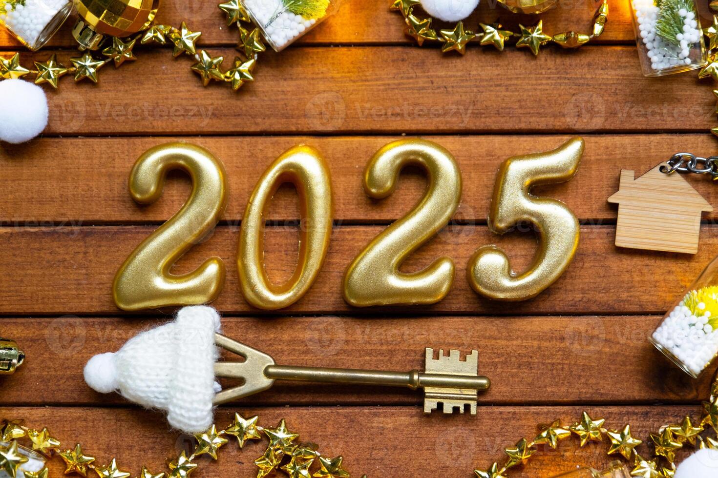 House key with tiny figure of home mock up on festive brown wooden background, lights of garlands. New Year 2025 wooden letters, greeting card. Purchase, construction, relocation, mortgage, insurance photo