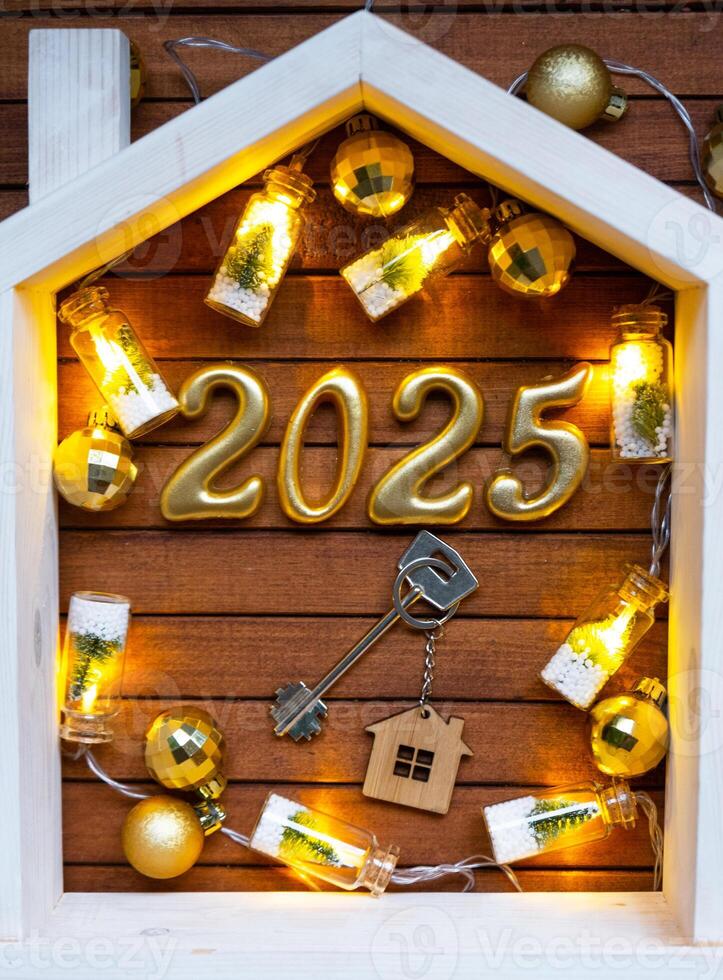 casa llave con llavero cabaña en festivo marrón de madera antecedentes con estrellas, luces de guirnaldas nuevo año 2025 dorado letras debajo el techo. compra, construcción, reubicación, hipoteca, seguro foto
