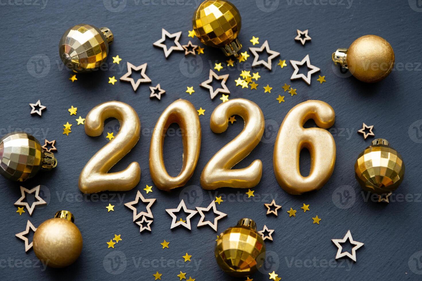 The golden figures 2026 made of candles on a black stone slate background are decorated with a festive decor of stars, sequins, fir branches, balls and garlands. Greeting card, happy New Year. photo