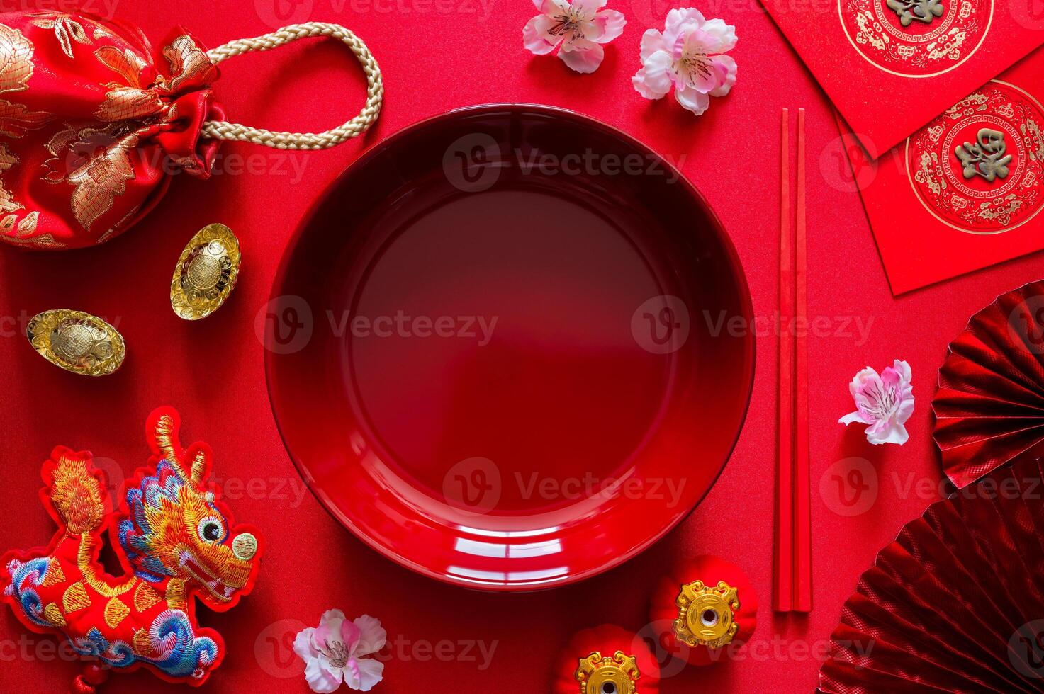 Red plate with chopstick on red cloth background with ingots word mean wealth, red bag, dragon pendant and red envelope packet or ang bao word mean blessing for Chinese new year dinner concept. photo
