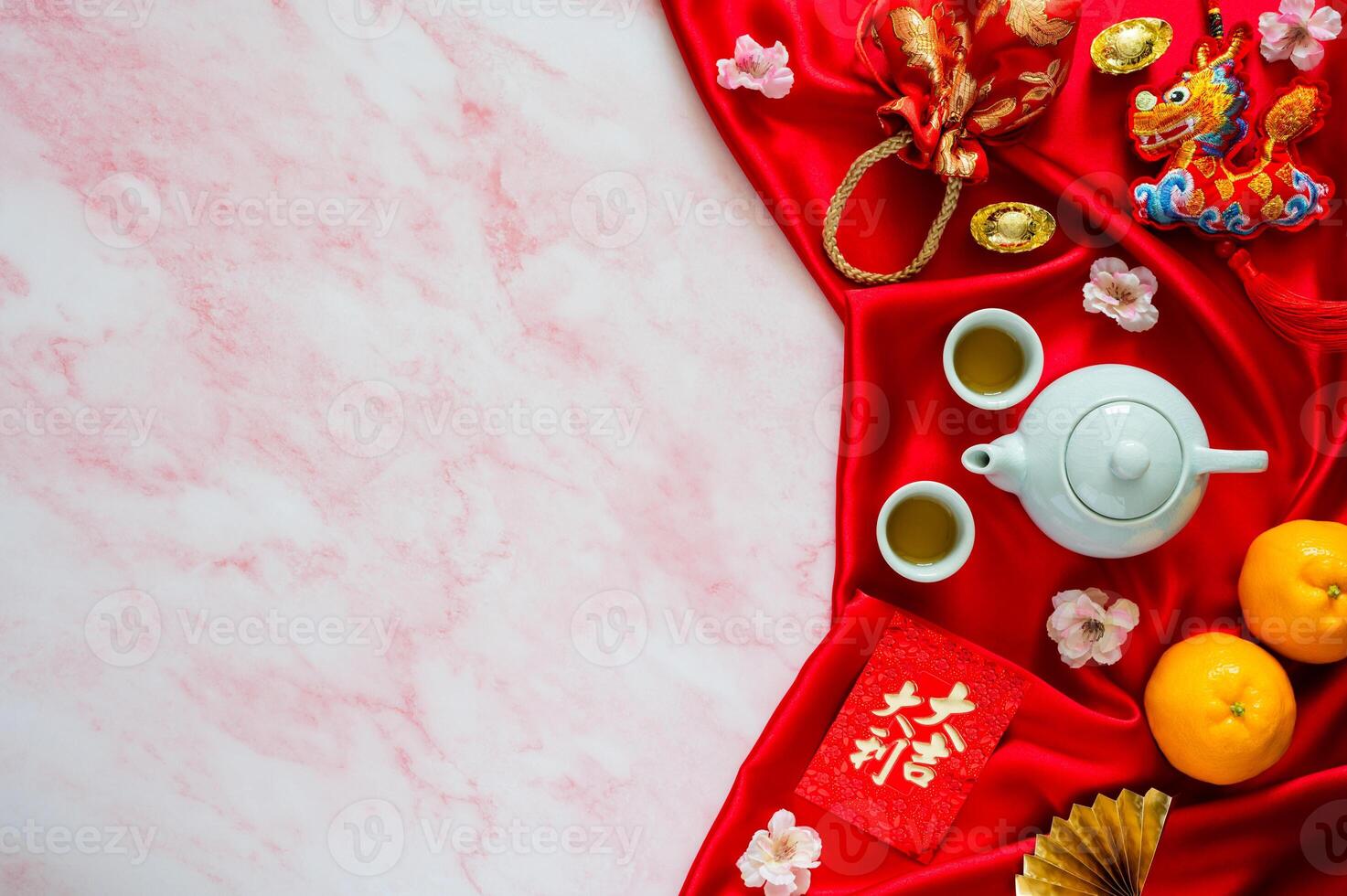 Tea set on red cloth background with red envelope packets or ang bao word mean auspice, red bag, ingots word mean wealth, hanging pendant dragon and oranges on marble table. photo