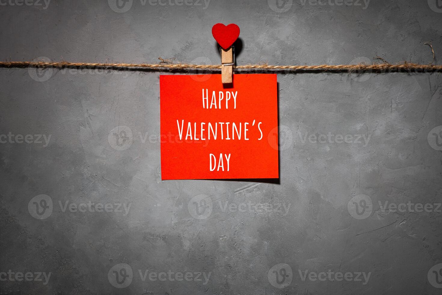 red paper with text Happy Valentines Day on a rope on a gray background. Background for a postcard photo