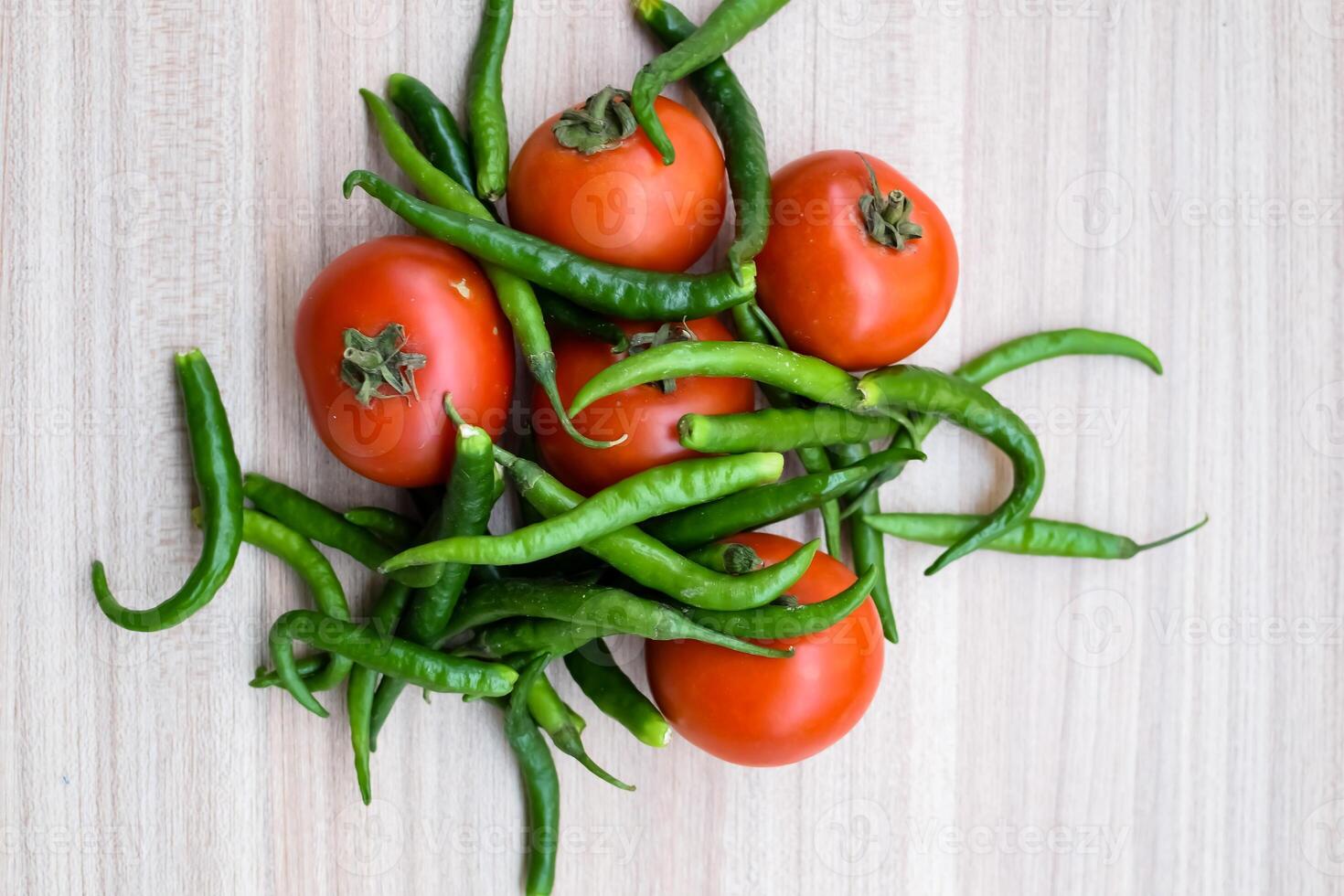 Red tomato and green chili pepper on plain wooden table, green essential vegetables for all essential foods, view of unpeeled vegetables with plain background photo