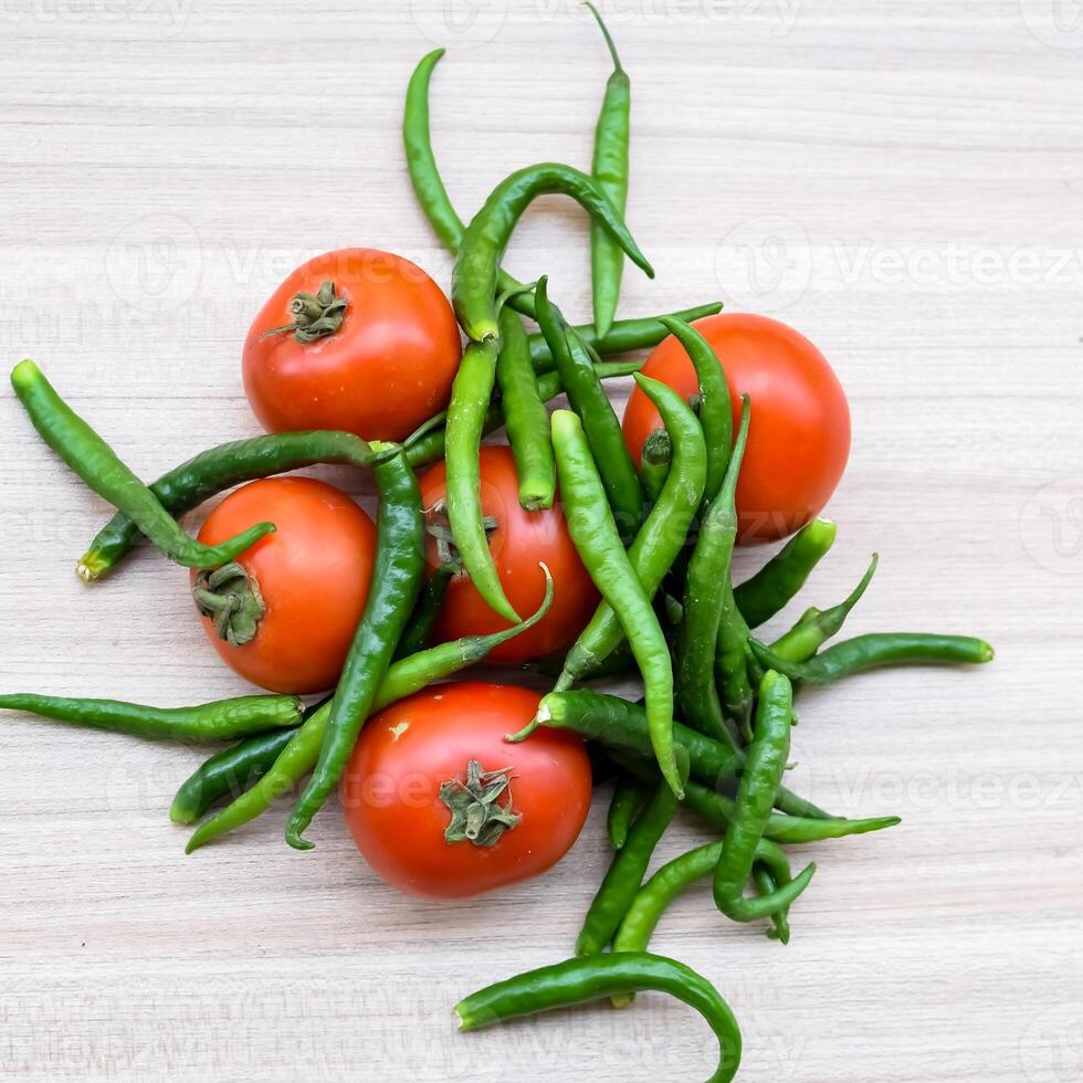 Red tomato and green chili pepper on plain wooden table, green essential vegetables for all essential foods, view of unpeeled vegetables with plain background photo