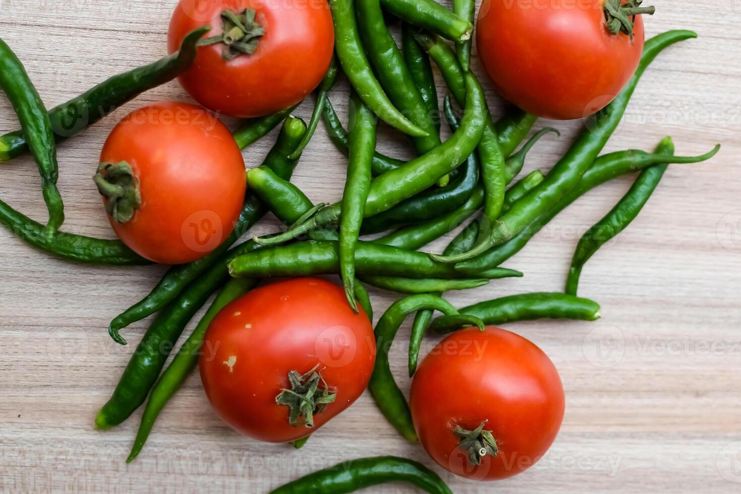 Red tomato and green chili pepper on plain wooden table, green essential vegetables for all essential foods, view of unpeeled vegetables with plain background photo