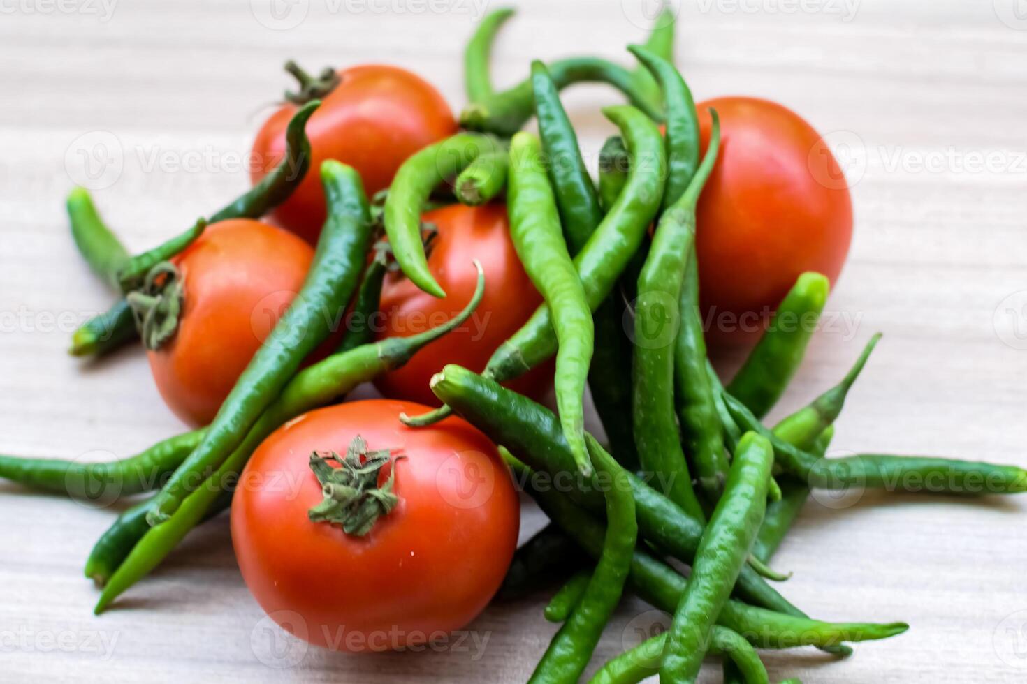 Red tomato and green chili pepper on plain wooden table, green essential vegetables for all essential foods, view of unpeeled vegetables with plain background photo