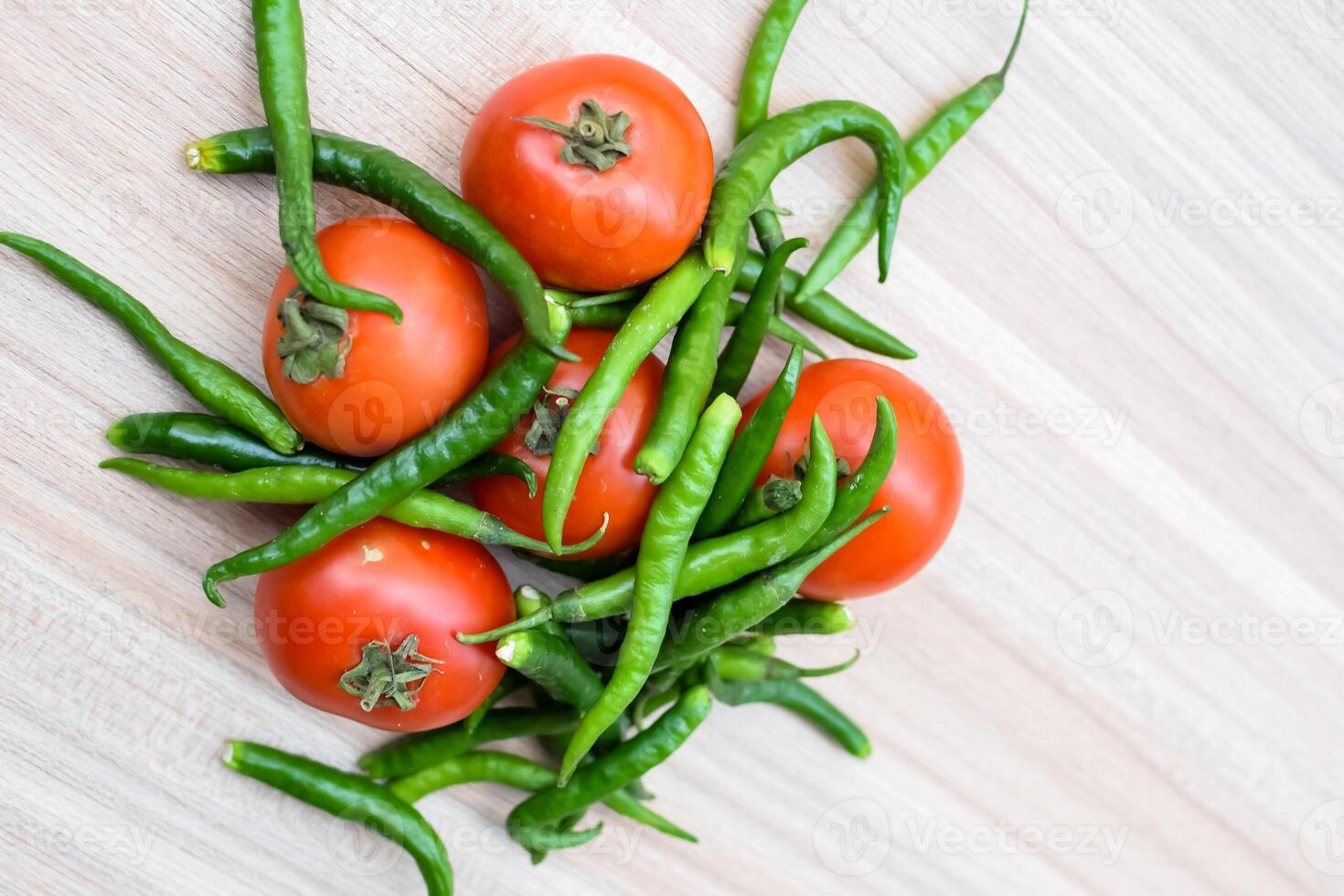 Red tomato and green chili pepper on plain wooden table, green essential vegetables for all essential foods, view of unpeeled vegetables with plain background photo