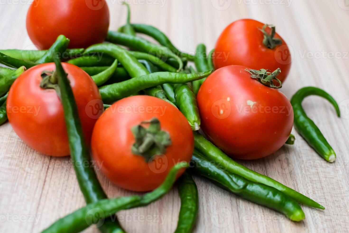 Red tomato and green chili pepper on plain wooden table, green essential vegetables for all essential foods, view of unpeeled vegetables with plain background photo