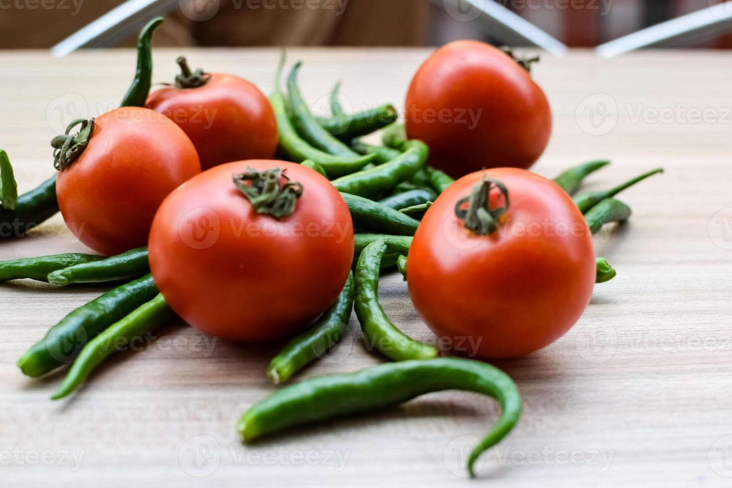Red tomato and green chili pepper on plain wooden table, green essential vegetables for all essential foods, view of unpeeled vegetables with plain background photo