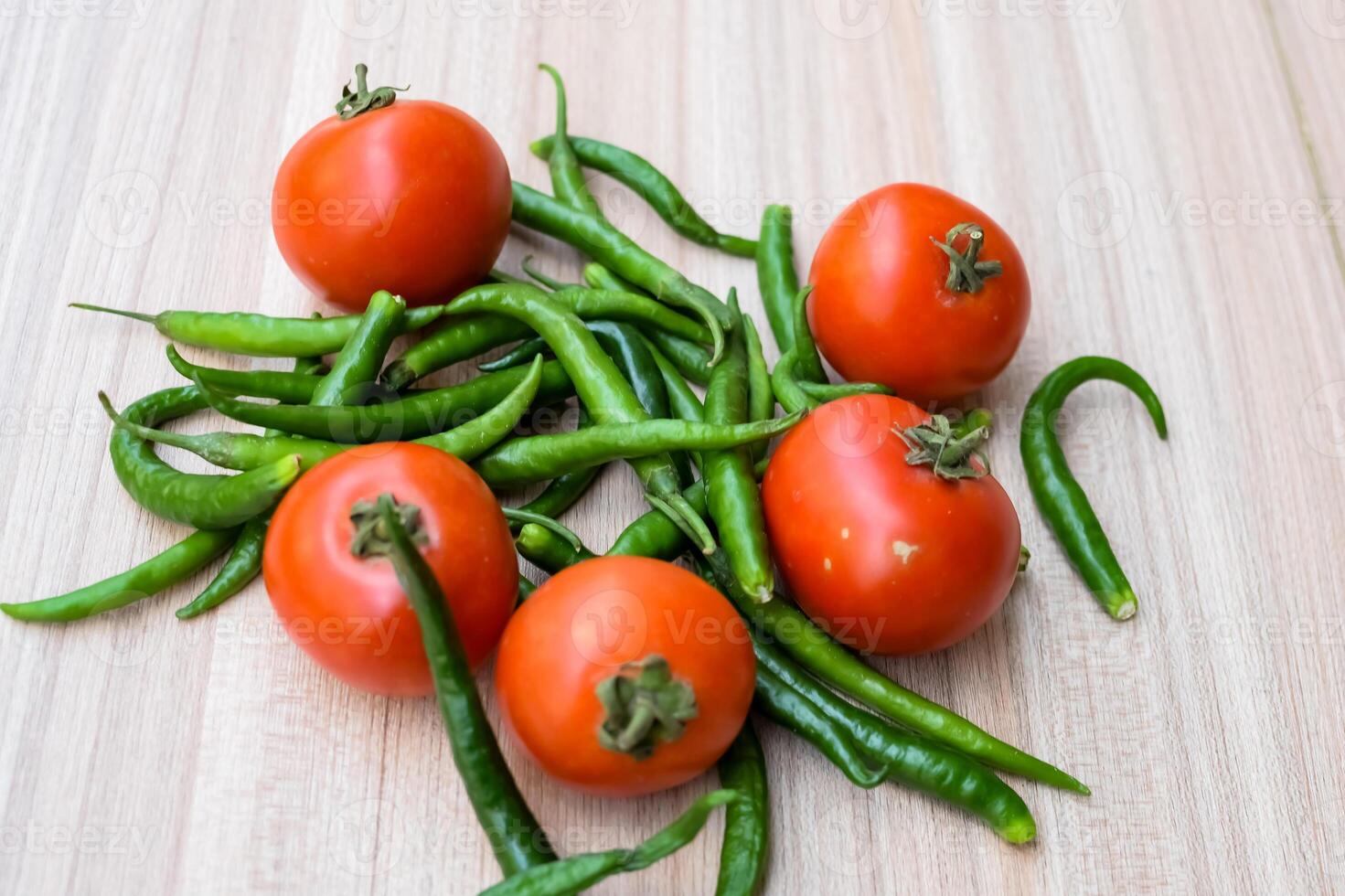 Red tomato and green chili pepper on plain wooden table, green essential vegetables for all essential foods, view of unpeeled vegetables with plain background photo