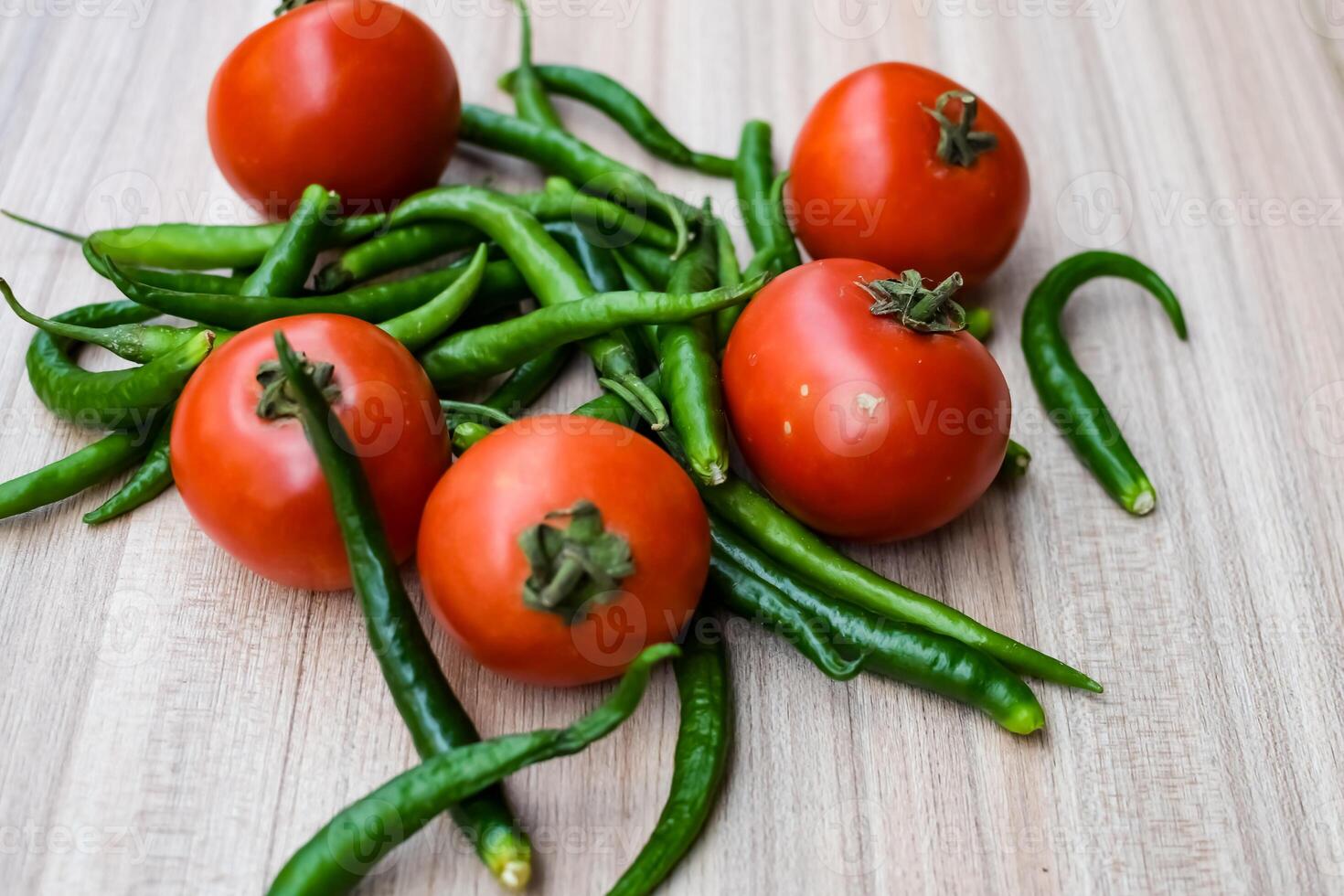 Red tomato and green chili pepper on plain wooden table, green essential vegetables for all essential foods, view of unpeeled vegetables with plain background photo