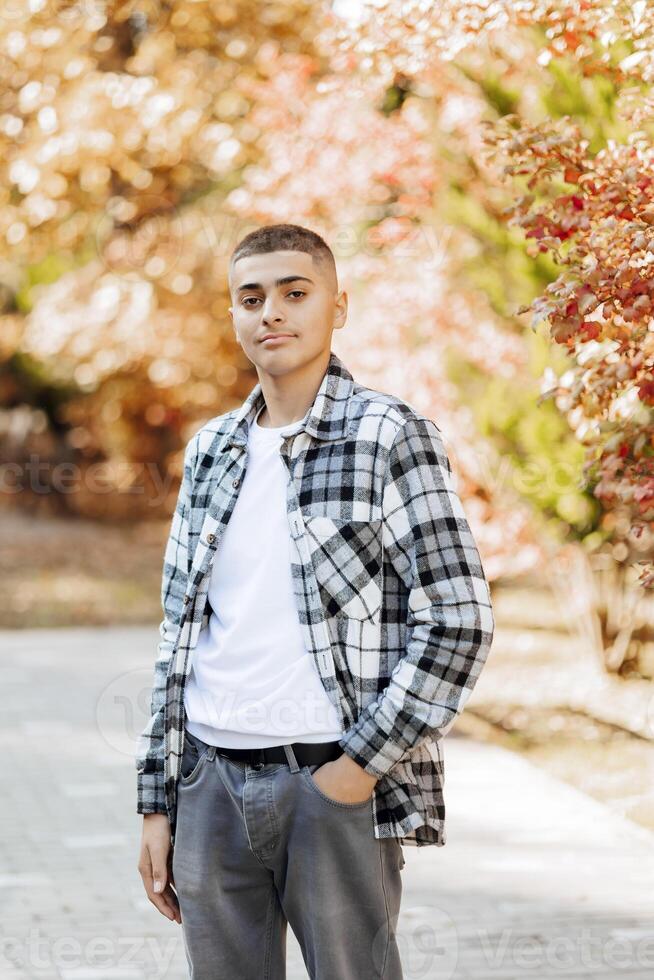 Vertical close-up portrait of a teenager in casual clothes. Happy smiling teenager in autumn park in sunlight. A beautiful child looks at the camera in nature. photo