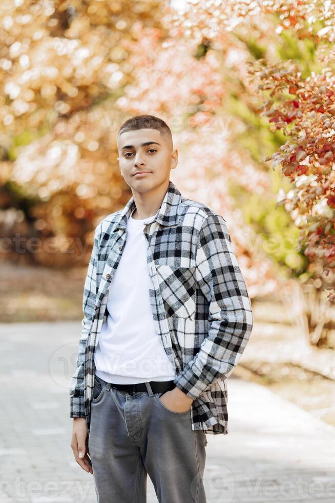 Vertical close-up portrait of a teenager in casual clothes. Happy smiling teenager in autumn park in sunlight. A beautiful child looks at the camera in nature. photo