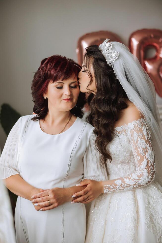 A beautiful and happy mother and her daughter, the bride, are standing next to each other. The best day for parents. Tender moments at the wedding. photo