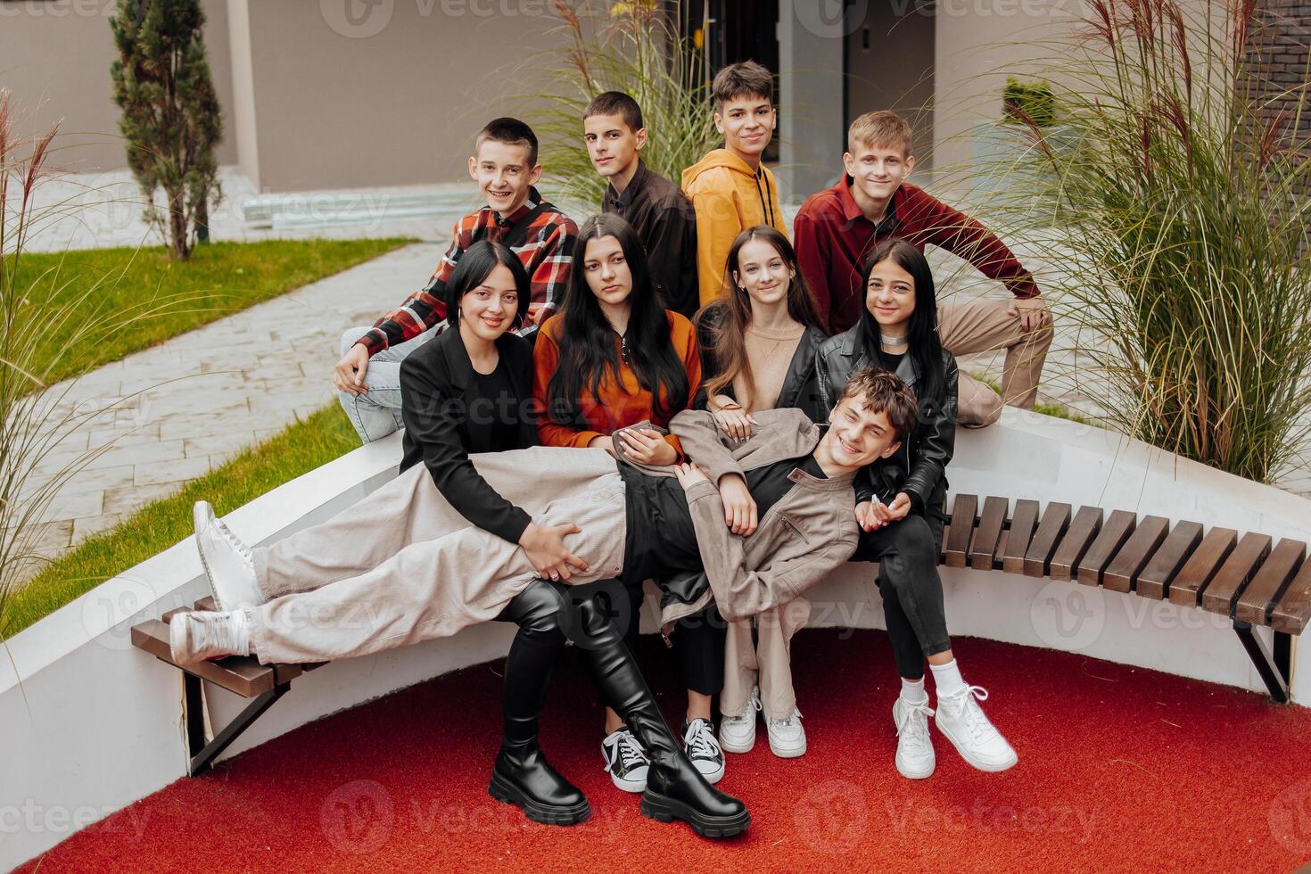 Group of smiling and happy teenage friends wearing casual clothes spending time together, posing and talking with each other near college building on autumn day. photo