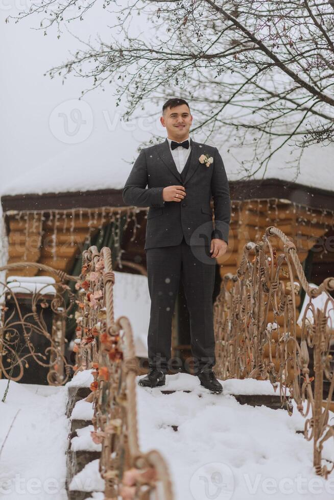 retrato de un hermoso novio en un invierno parque. el novio en un elegante traje va a el Boda ceremonia foto