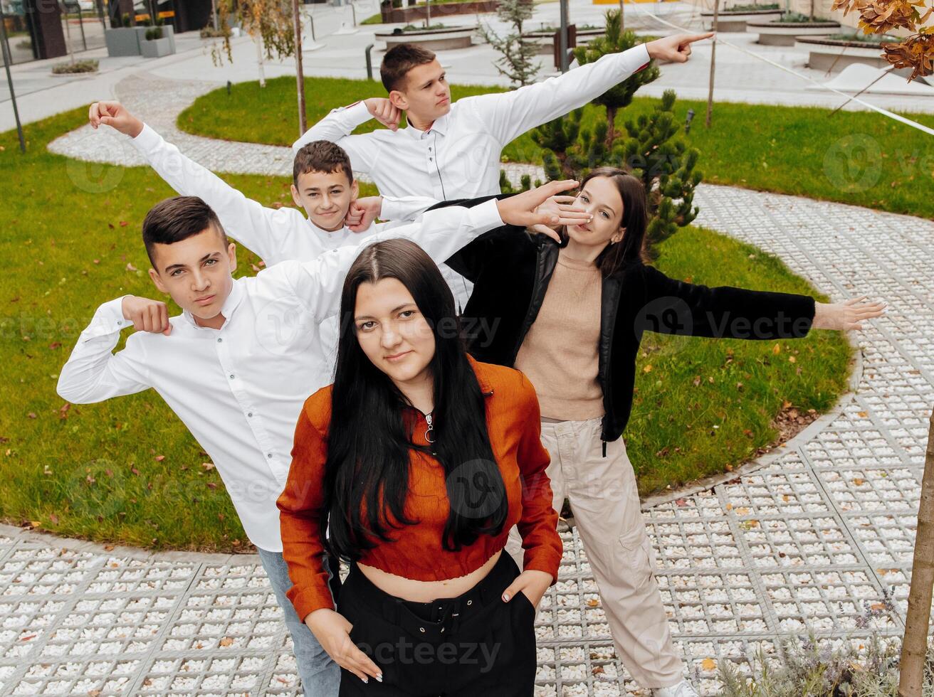 A group of smiling and happy teenage friends, dressed in casual clothes, spend time together, pose and have fun on the grounds of an educational institution on an autumn day. photo