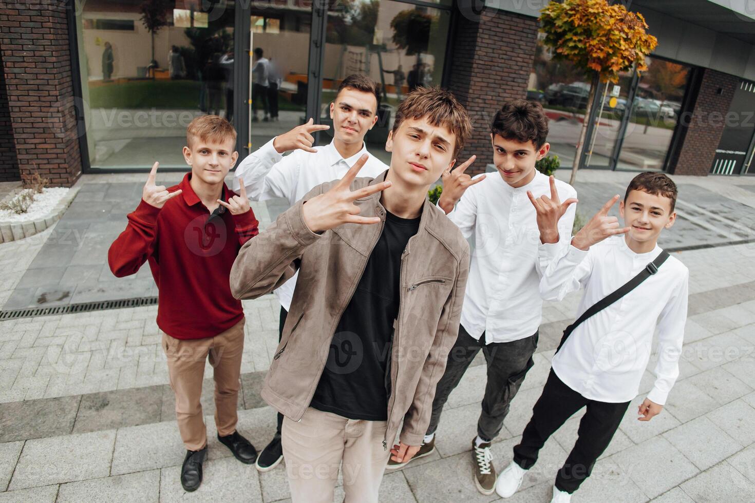 Group of smiling and happy teenage friends wearing casual clothes spending time together, posing and talking with each other near college building on autumn day. photo