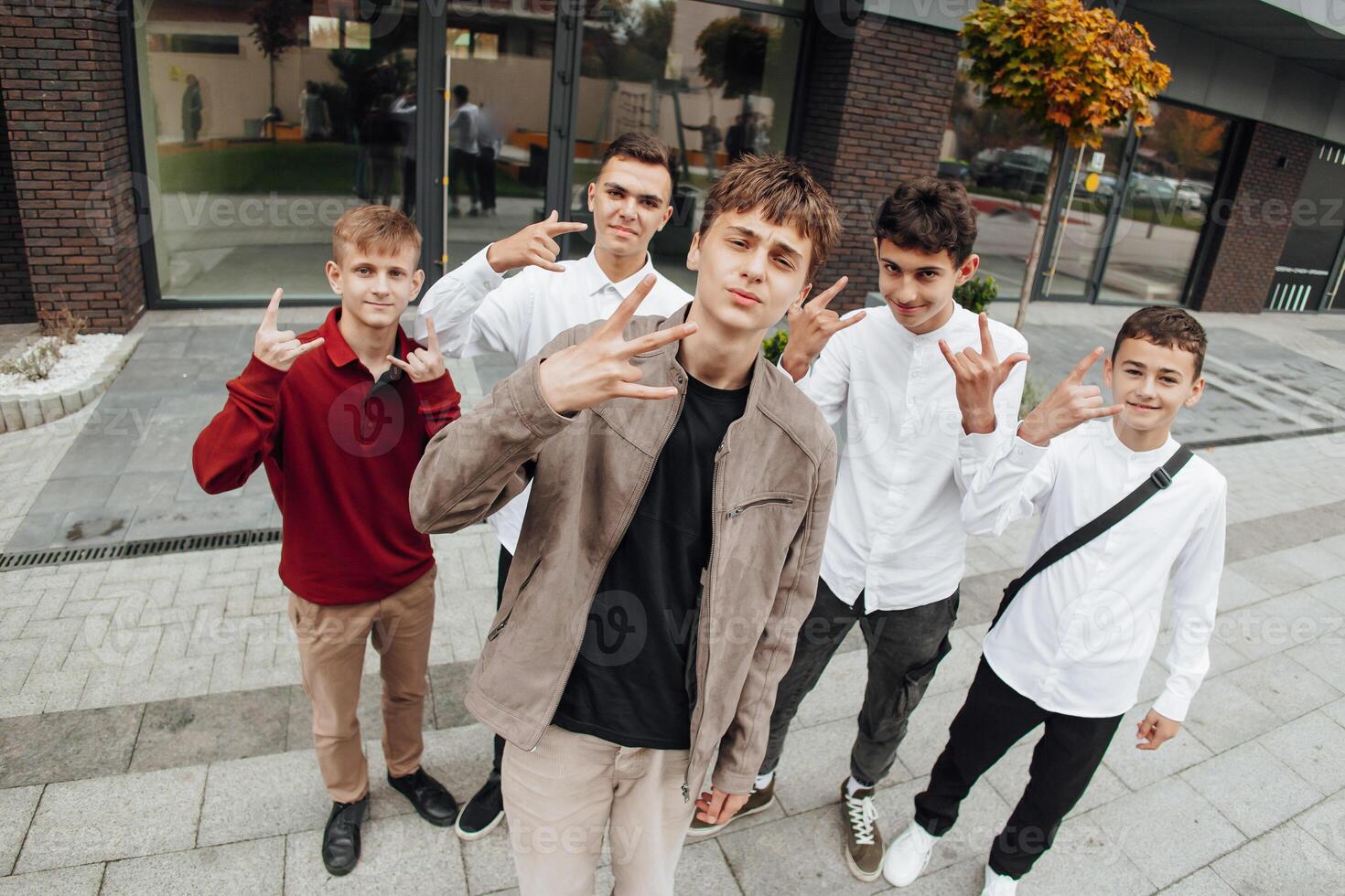 grupo de sonriente y contento Adolescente amigos vistiendo casual ropa gasto hora juntos, posando y hablando con cada otro cerca Universidad edificio en otoño día. foto