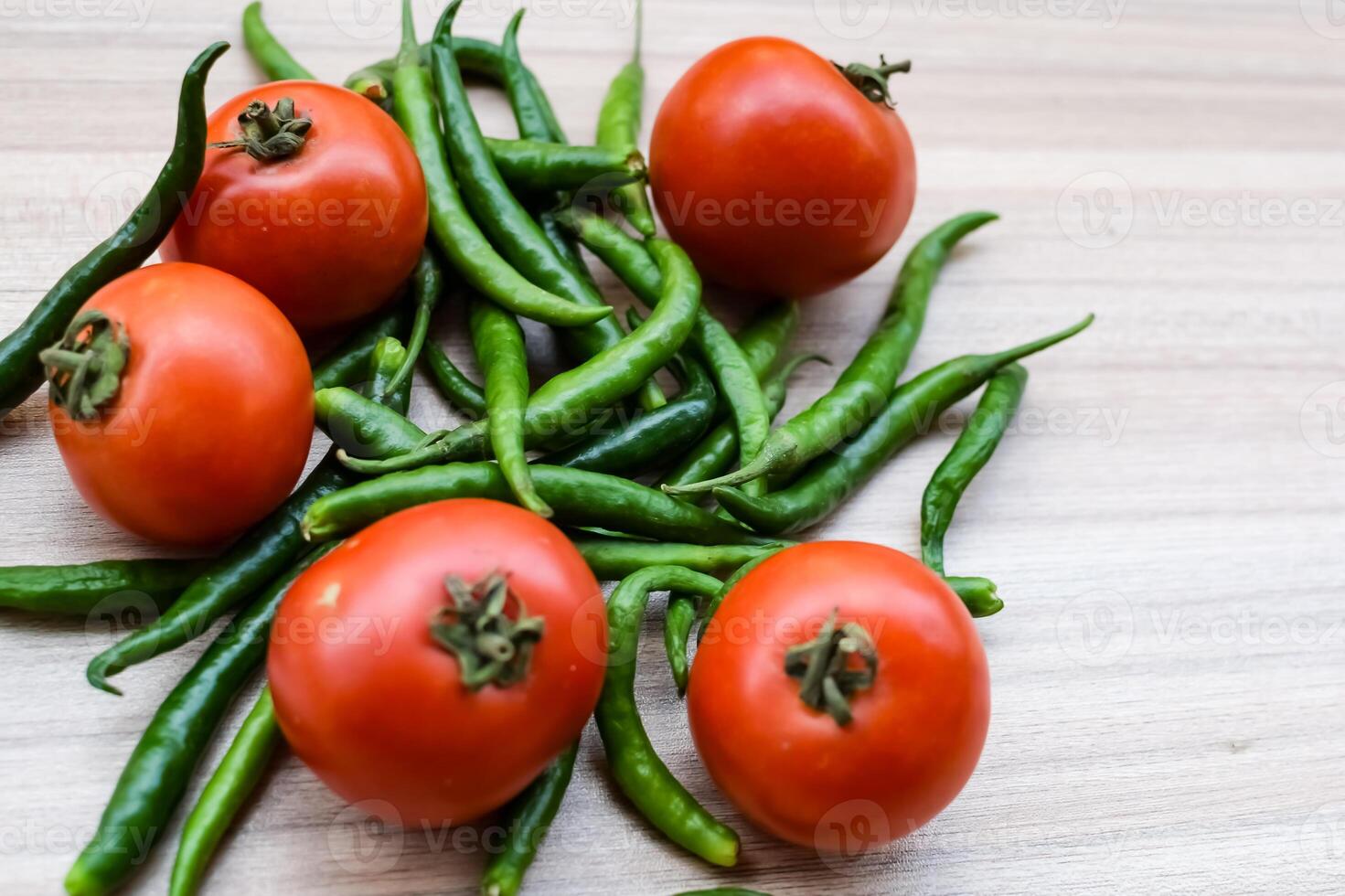 Red tomato and green chili pepper on plain wooden table, green essential vegetables for all essential foods, view of unpeeled vegetables with plain background photo