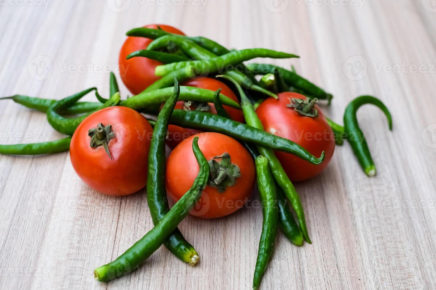 Red tomato and green chili pepper on plain wooden table, green essential vegetables for all essential foods, view of unpeeled vegetables with plain background photo