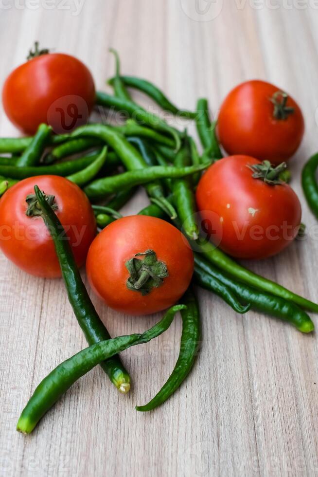 Red tomato and green chili pepper on plain wooden table, green essential vegetables for all essential foods, view of unpeeled vegetables with plain background photo