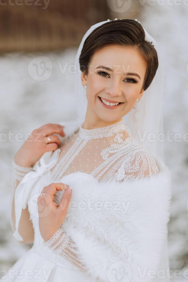 The bride poses during a walk in winter, wrapped in a poncho. Exquisite dress and hairstyle. photo
