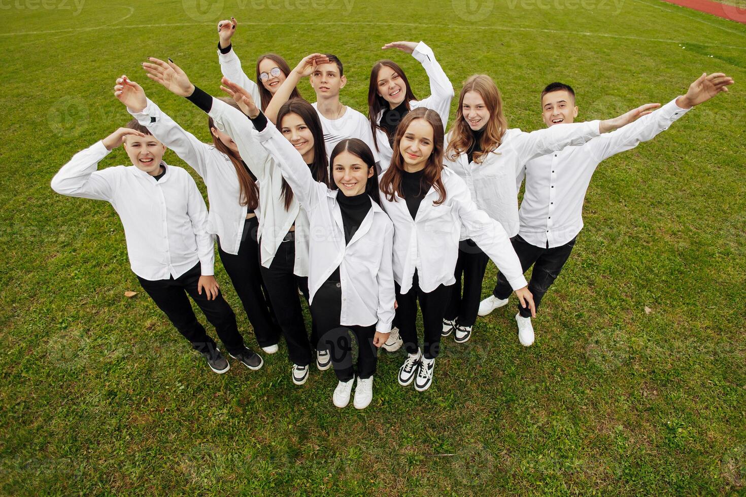 A group of many happy teenagers dressed in the same outfit having fun and posing in a stadium near a college. Concept of friendship, moments of happiness. School friendship photo