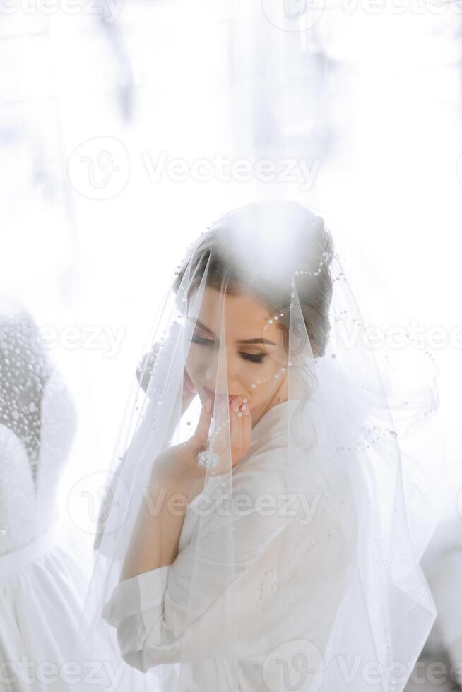 A beautiful brunette bride with a tiara in her hair is getting ready for the wedding in a beautiful robe in boudoir style. Close-up wedding portrait, photo. photo