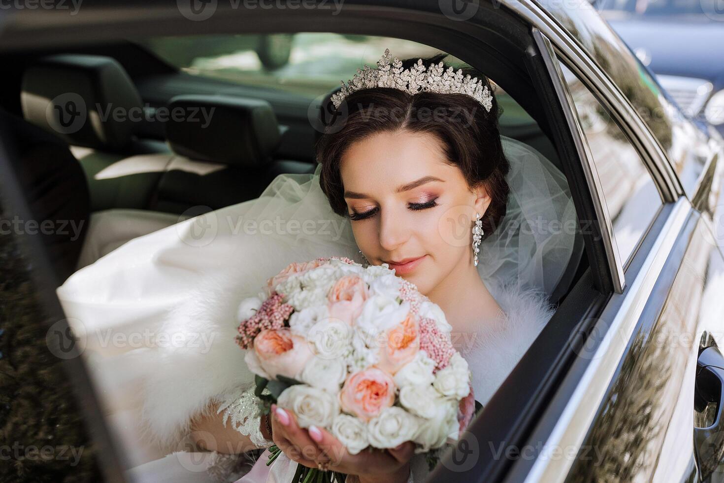 Portrait of an incredibly beautiful bride in the window of an expensive car. The bride with a bouquet of flowers tenderly looks at the flowers. photo