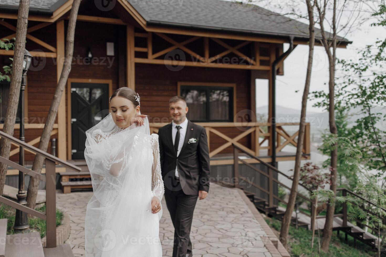 retrato. un novia en un elegante largo vestir y velo y un novio en un traje actitud mientras en pie cerca arboles Boda en naturaleza foto