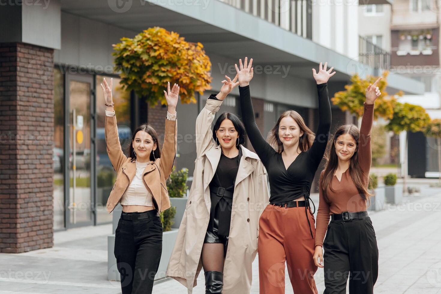 Group of smiling and happy teenage friends wearing casual clothes spending time together, posing and talking with each other near college building on autumn day. photo
