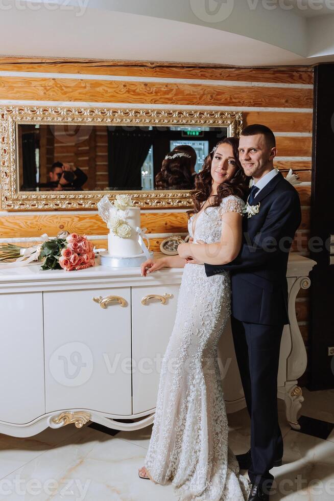 Wedding. Groom and bride near the wedding cake. A sweet and delicious dessert for a wedding. The bride cuts the wedding cake with the help of her lover. The groom embraces his beloved. photo