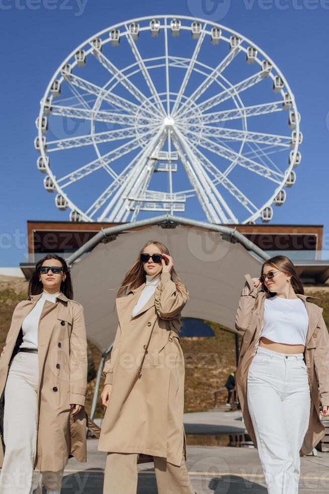 Three beautiful young teenage girls having fun together outdoors against the background of a ferris wheel in an Italian town. Urban lifestyle. City center. Best friends in casual clothes. photo