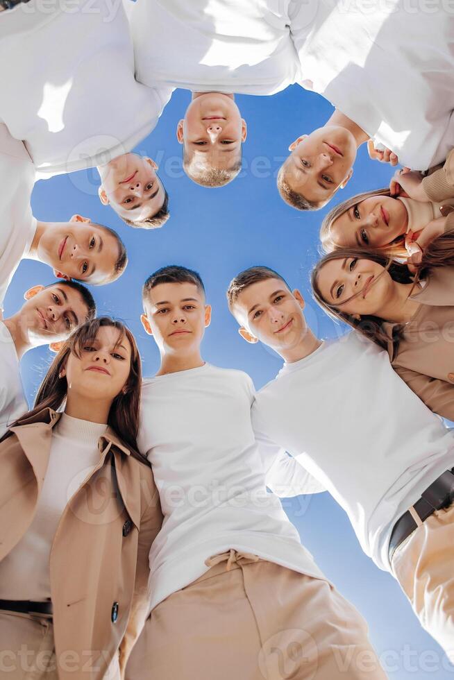 Large group of smiling young people standing, hugging, looking at camera. Group of cheerful teenage people in a circle looking down. Low viewing angle. Copy space. photo