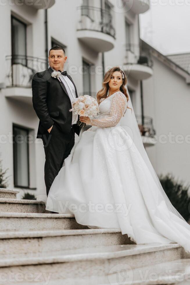 el novia y novio son caminando cerca el hotel y posando, contento y disfrutando el día, participación manos. un largo tren en el vestido. invierno Boda foto