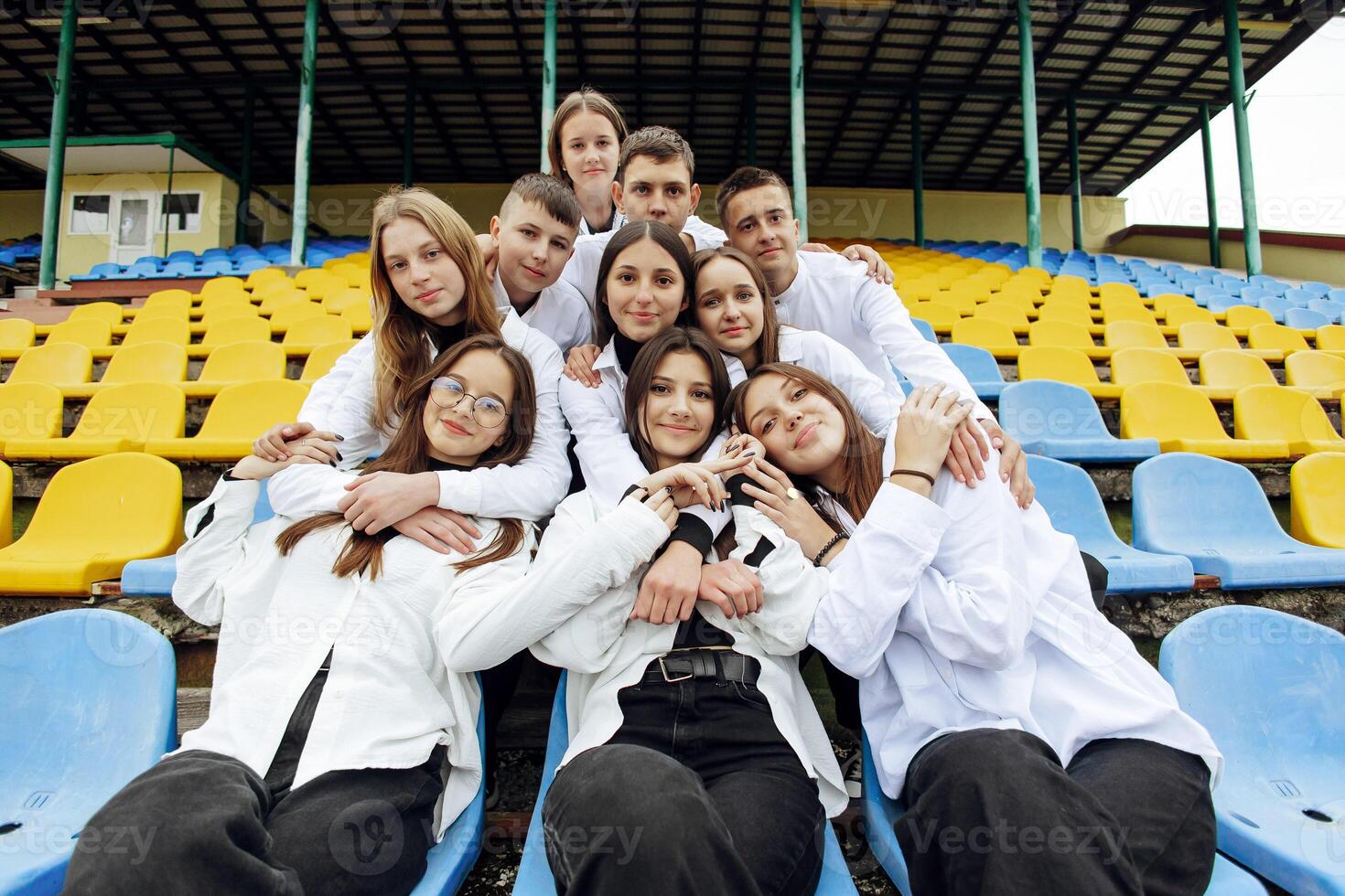 A group of many happy teenagers dressed in the same outfit having fun and posing in a stadium near a college. Concept of friendship, moments of happiness. School friendship photo