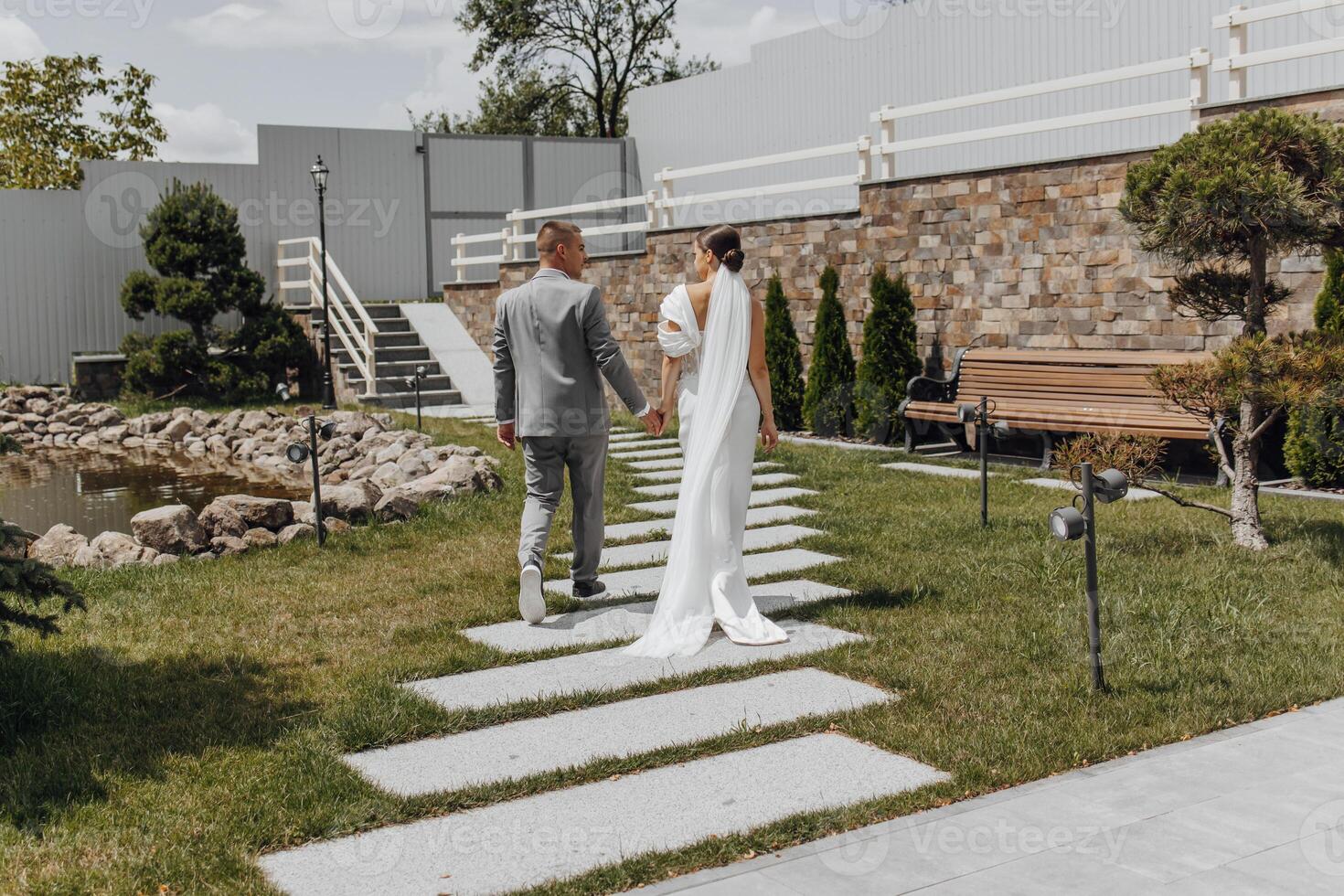 Full length portrait of young bride and groom running on green grass, rear view. Happy wedding couple walking, copy space photo