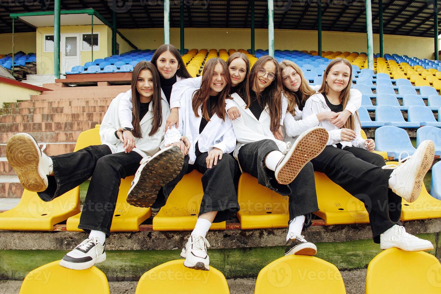 A group of many happy teenagers dressed in the same outfit having fun and posing in a stadium near a college. Concept of friendship, moments of happiness. School friendship photo