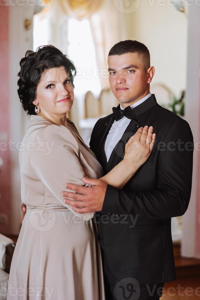 mother helps her adult son prepare for the wedding ceremony. An emotional and touching moment at a wedding. A mother hugs her son photo