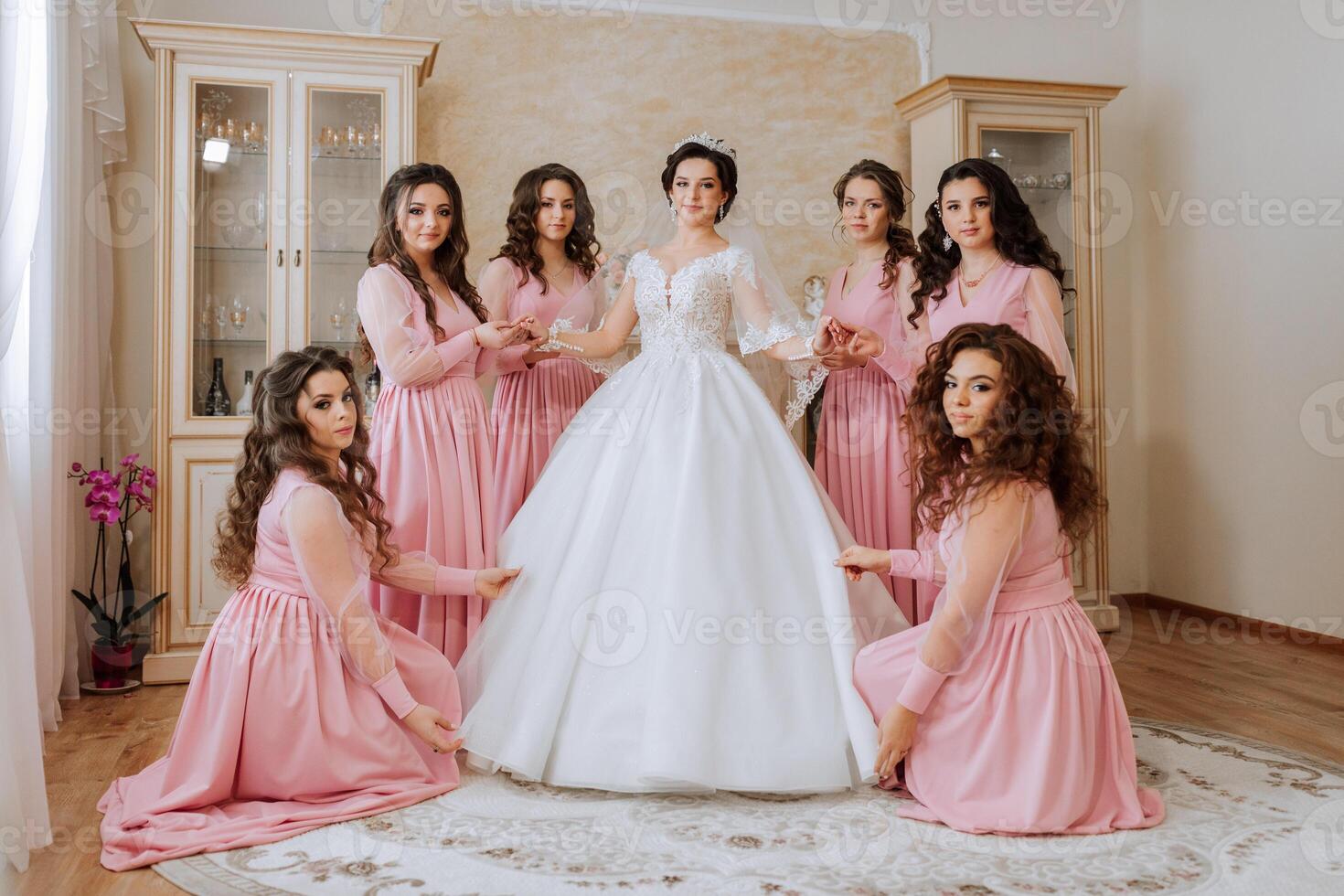 retrato de el novia con su amigos en el habitación. un morena novia en un largo blanco vestir y su amigos en rosado vestidos son sonriente y contento. joven chicas. foto