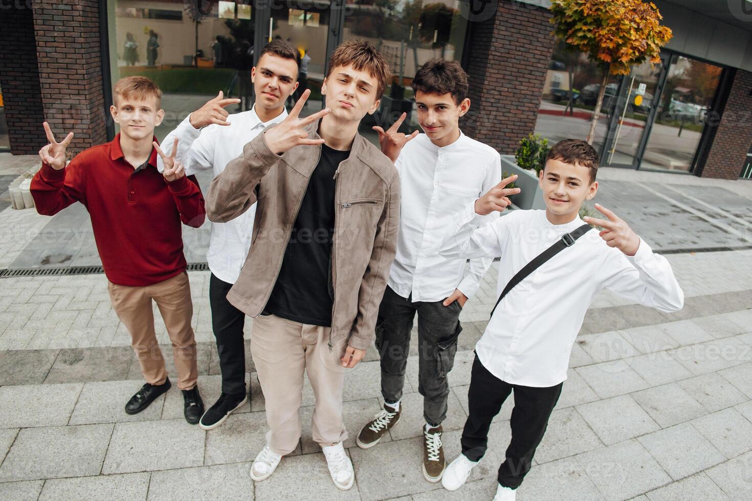Group of smiling and happy teenage friends wearing casual clothes spending time together, posing and talking with each other near college building on autumn day. photo