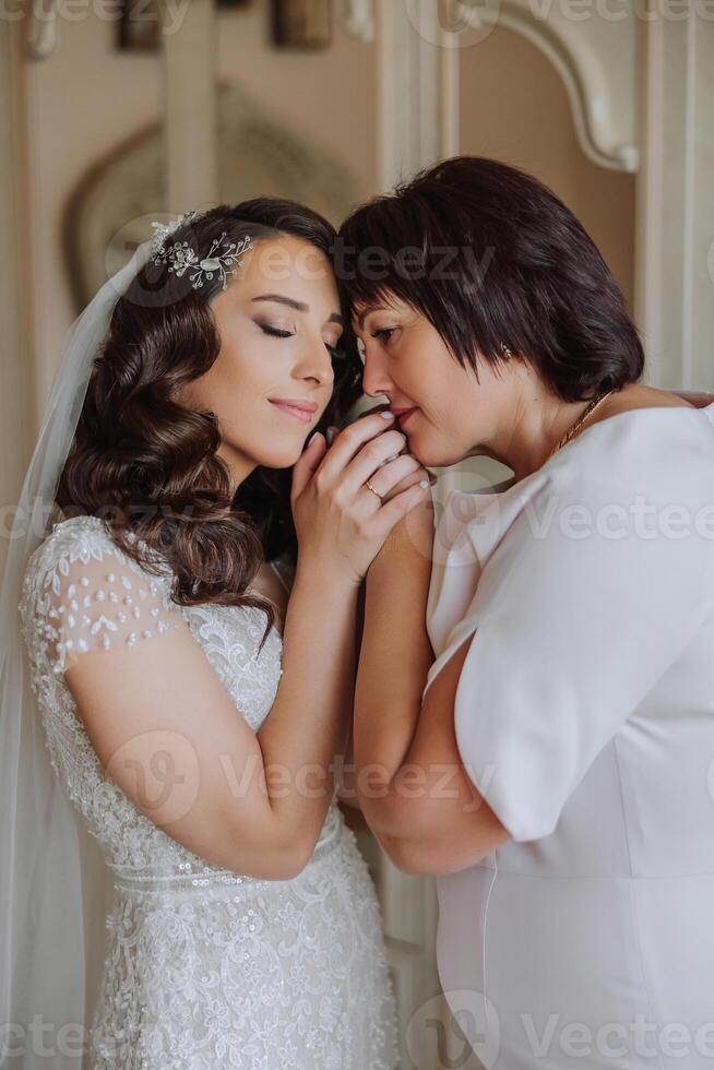 A beautiful and happy mother and her daughter, the bride, are standing next to each other. The best day for parents. Tender moments at the wedding. photo