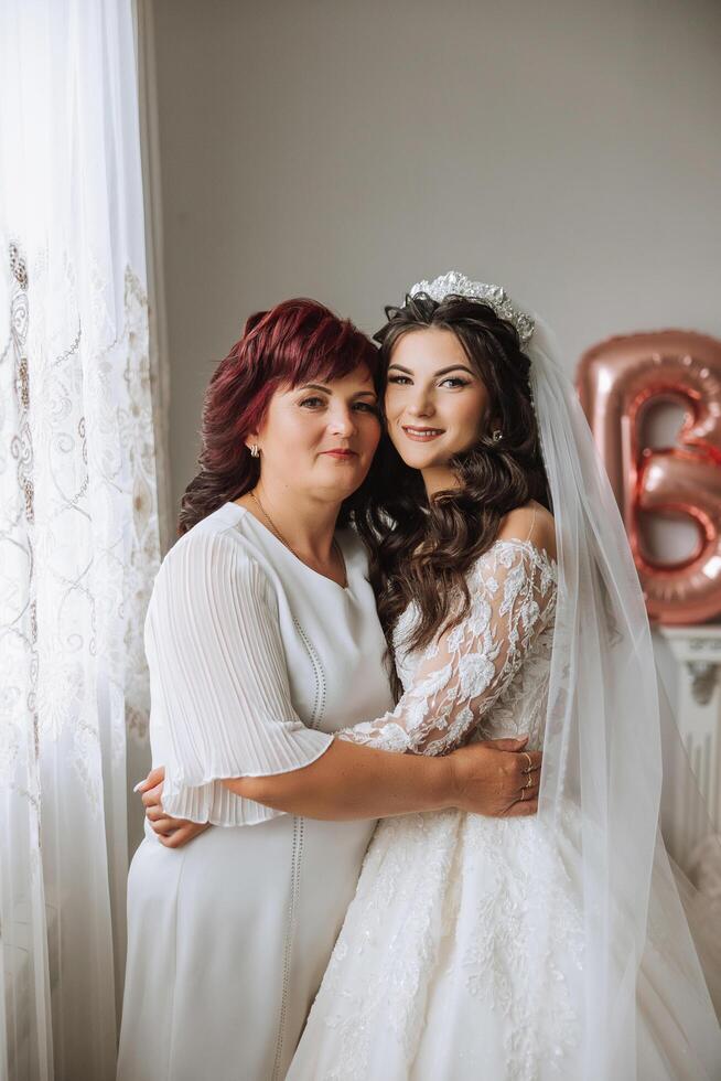 A beautiful and happy mother and her daughter, the bride, are standing next to each other. The best day for parents. Tender moments at the wedding. photo