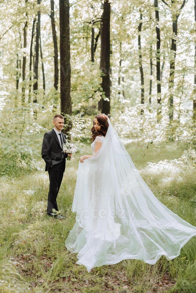 A beautiful young bride, in a summer park, walks ahead of her groom. Beautiful wedding white dress. Walks in the park. A happy and loving couple. photo