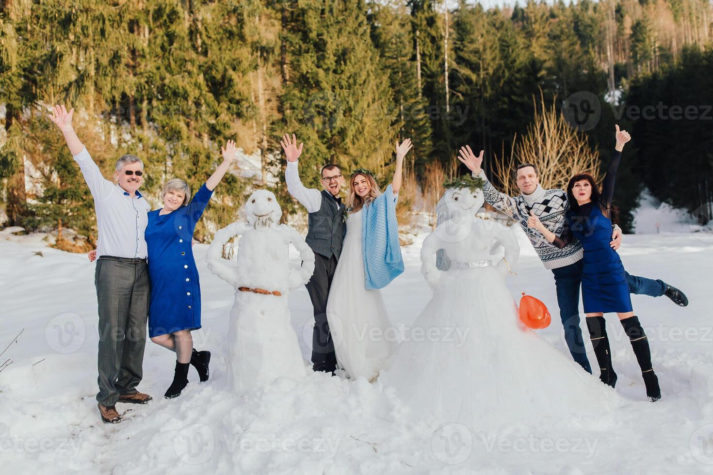 el novia y novio hecho muñecos de nieve con su padres. adultos además saber cómo a tener divertida. Boda en invierno en contra el antecedentes de un pino bosque. foto