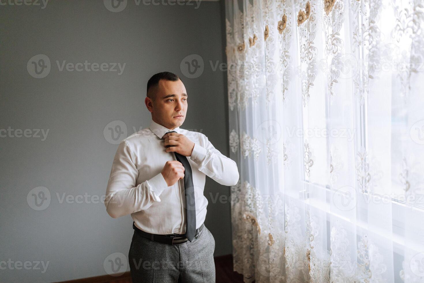 A man in a white shirt adjusts his tie. Business style. The groom on his wedding day photo