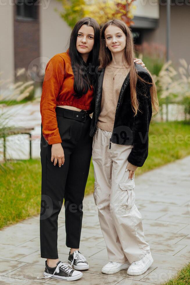 Vertical photo of two teenage friends dressed in casual clothes standing next to each other against a background of nature. Best school friends are ready to overcome anything to achieve the goal.