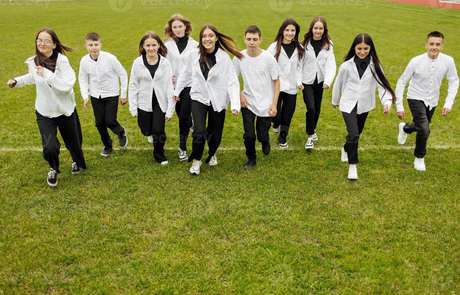 A group of many happy teenagers dressed in the same outfit having fun and posing in a stadium near a college. Concept of friendship, moments of happiness. School friendship photo